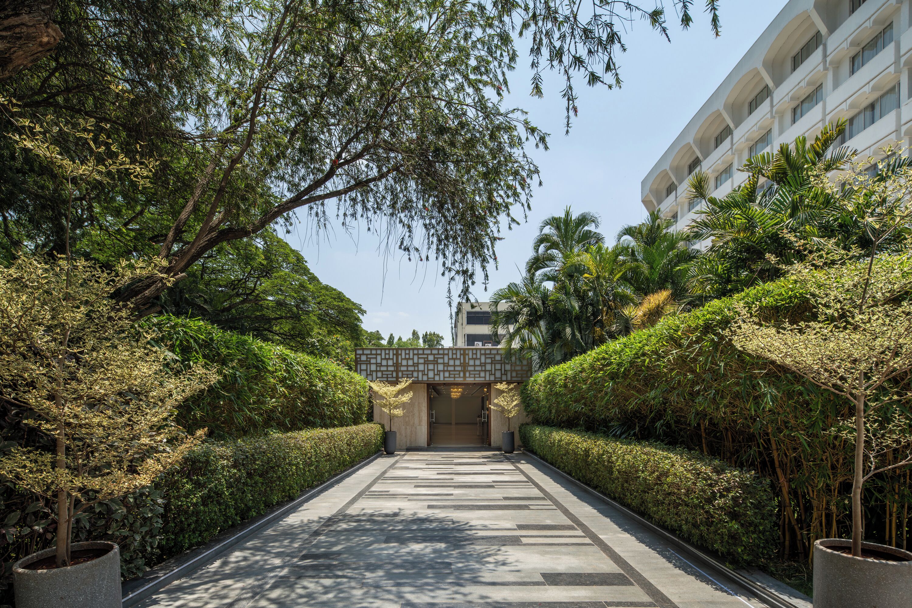 Un chemin menant à un bâtiment à l’architecture moderne, entouré de haies et d’arbres bien entretenus.