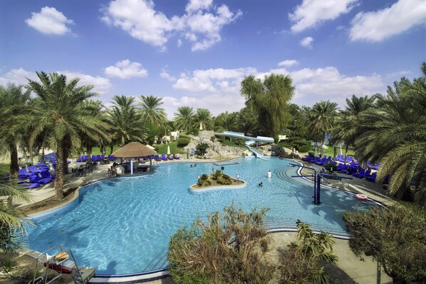 A large outdoor swimming pool surrounded by palm trees and blue lounge chairs.