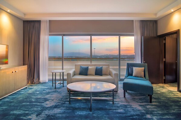 A hotel room with a large window, a sofa, a chair, a small table, and a cabinet.