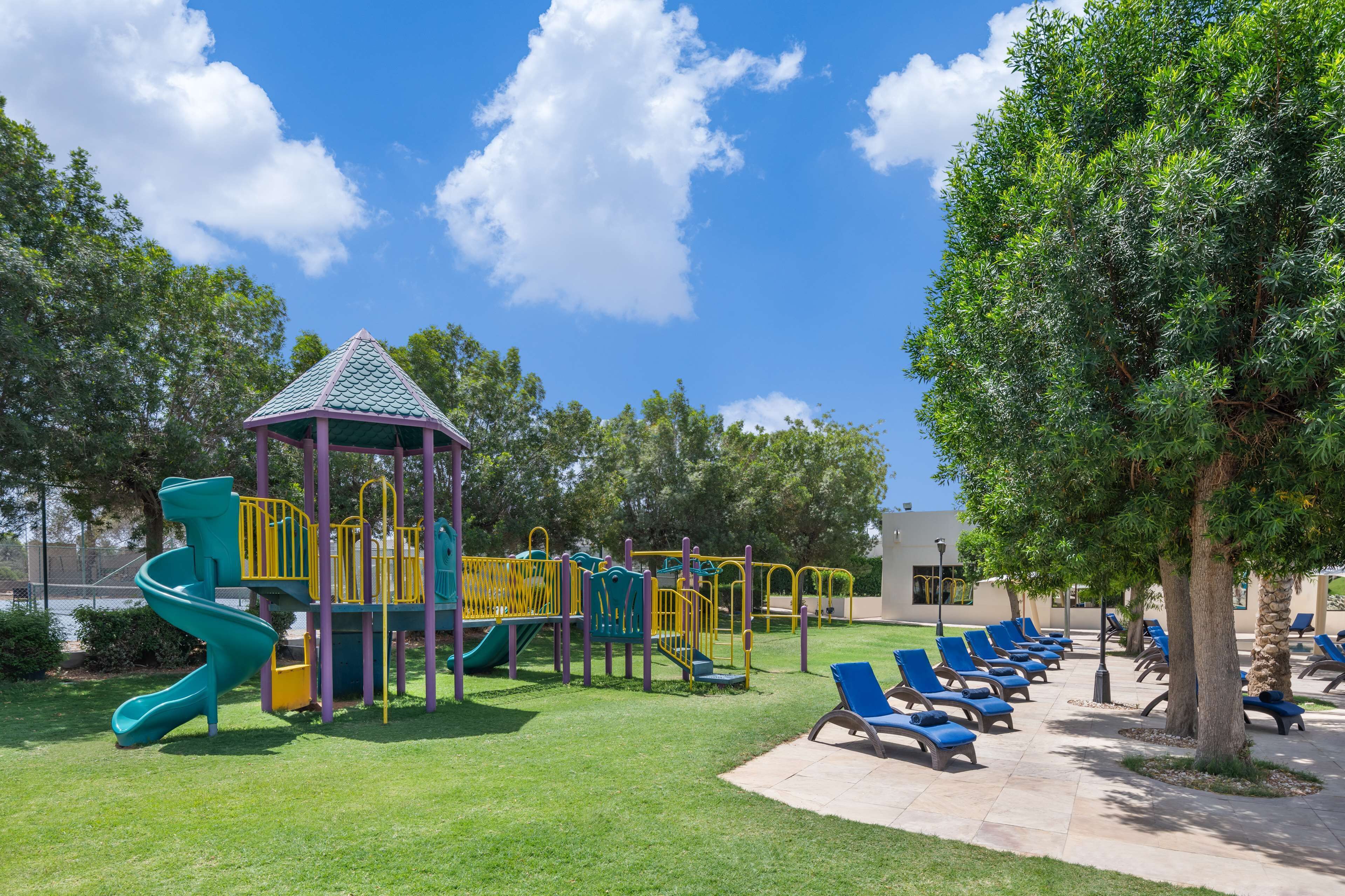 A playground with a slide and climbing structures, surrounded by a lawn and lounge chairs.