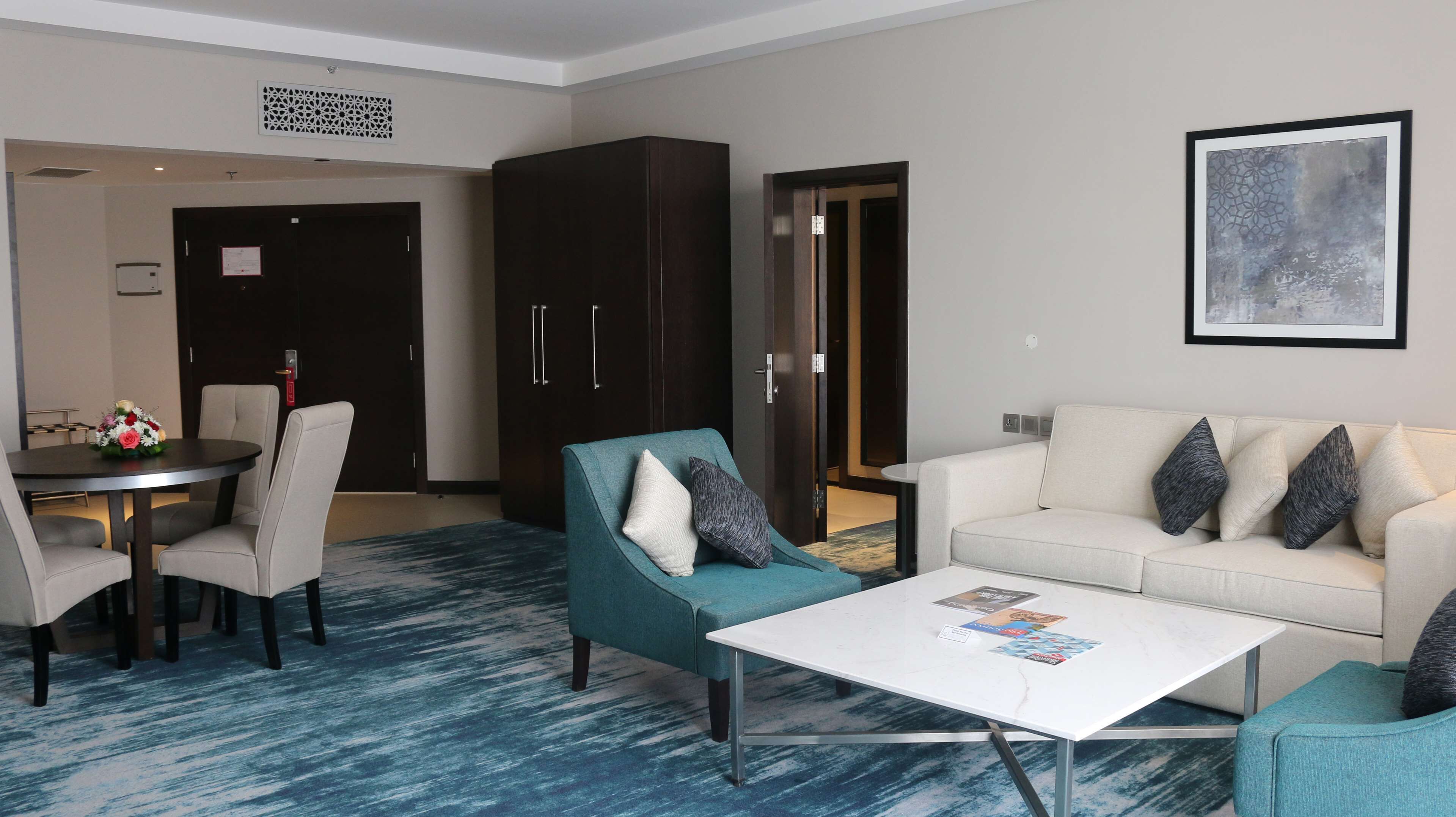 A modern hotel room with a dining area, a sofa set, and a coffee table.