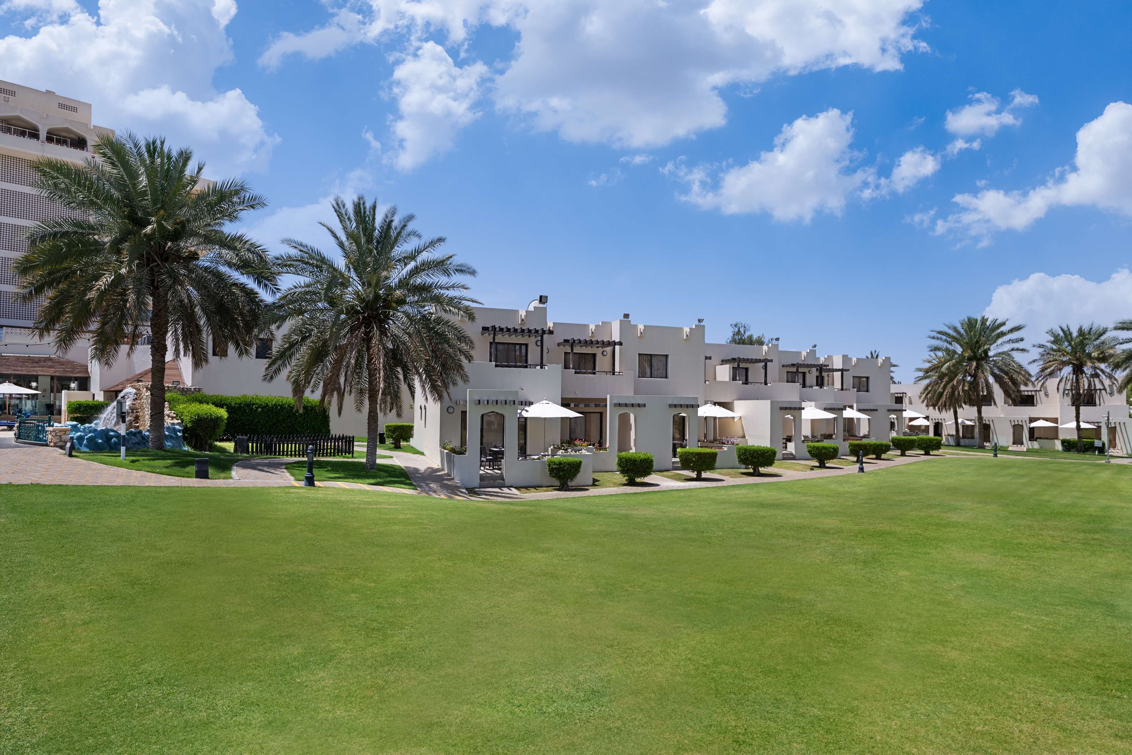 A hotel with a spacious courtyard, palm trees, and white buildings with multiple balconies.