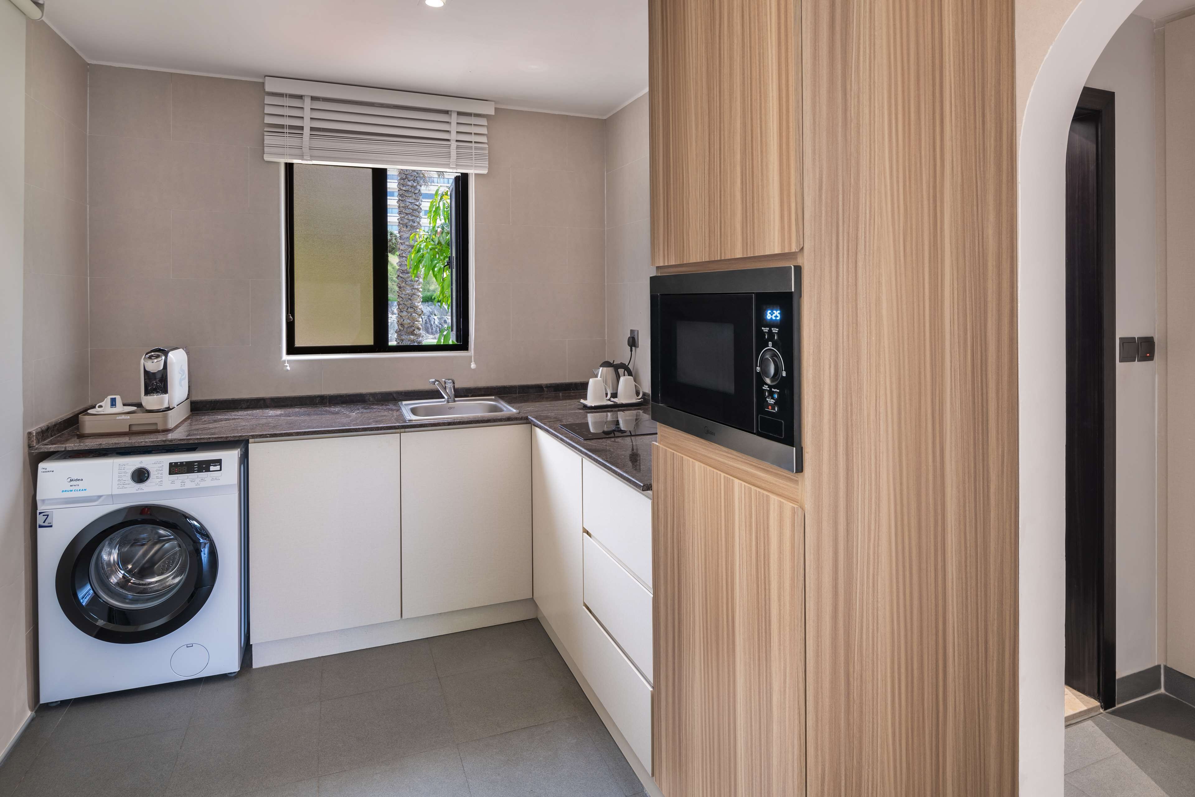 Una cocina compacta con lavadora integrada, microondas y ventana con persianas.