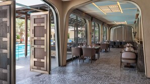 Ein Restaurant mit modernem Interieur, das einen gemusterten Boden, Holztüren mit Metallelementen und einen Blick auf den Außenbereich zeigt.