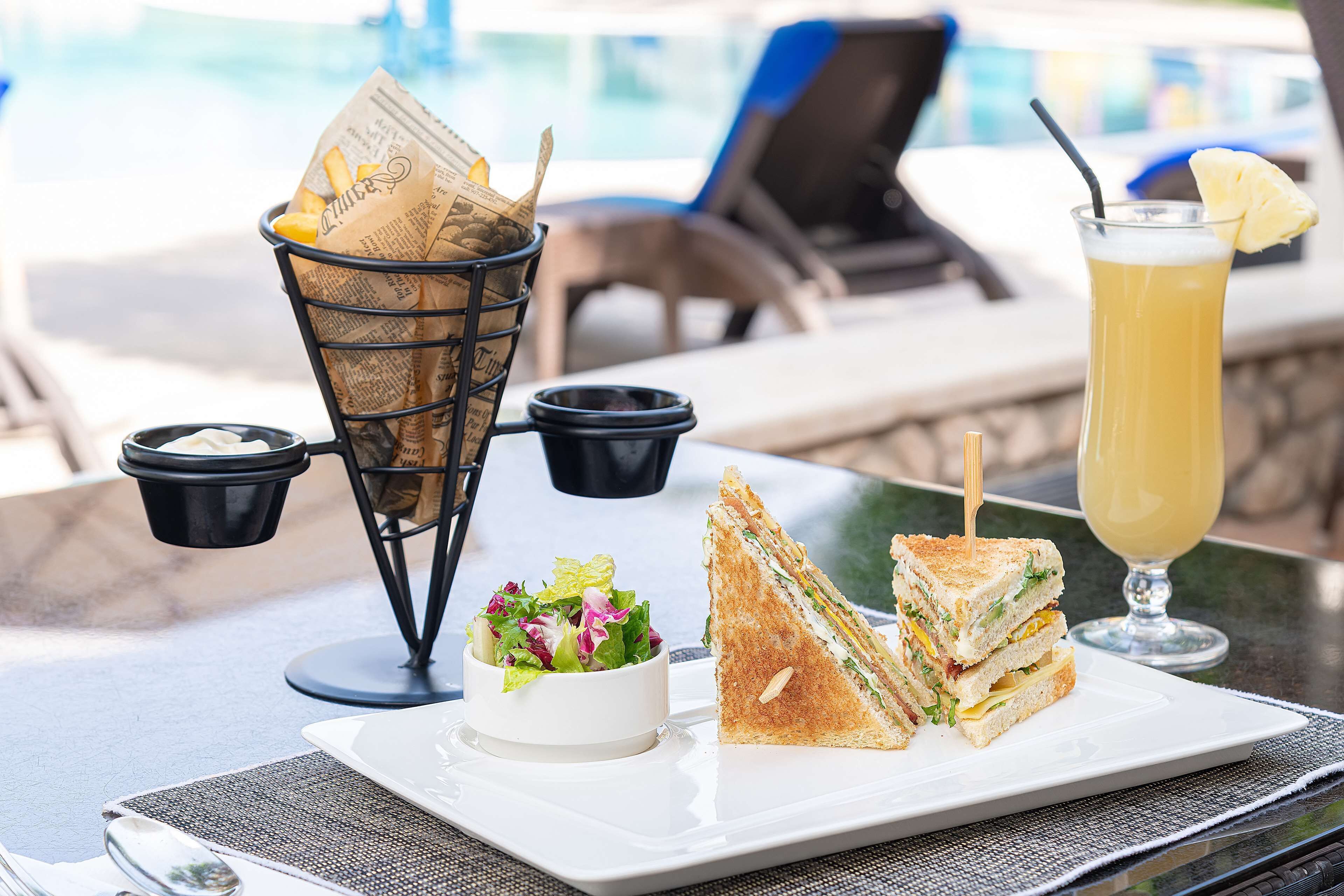 A table with a sandwich, a drink, a bowl of salad, and a basket of fries.
