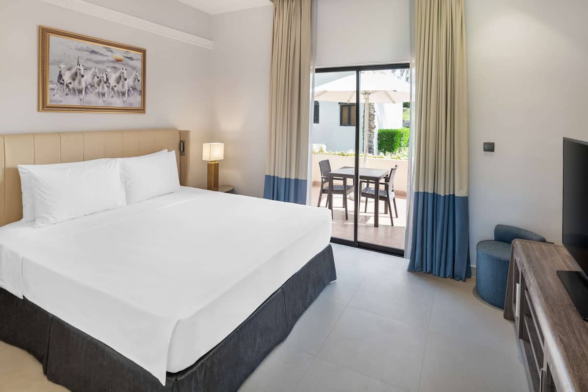 A hotel room with a large bed, a desk, a chair, and a television.