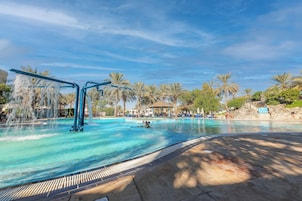 Piscina con fuente acuática, rodeada de palmeras y un pabellón.