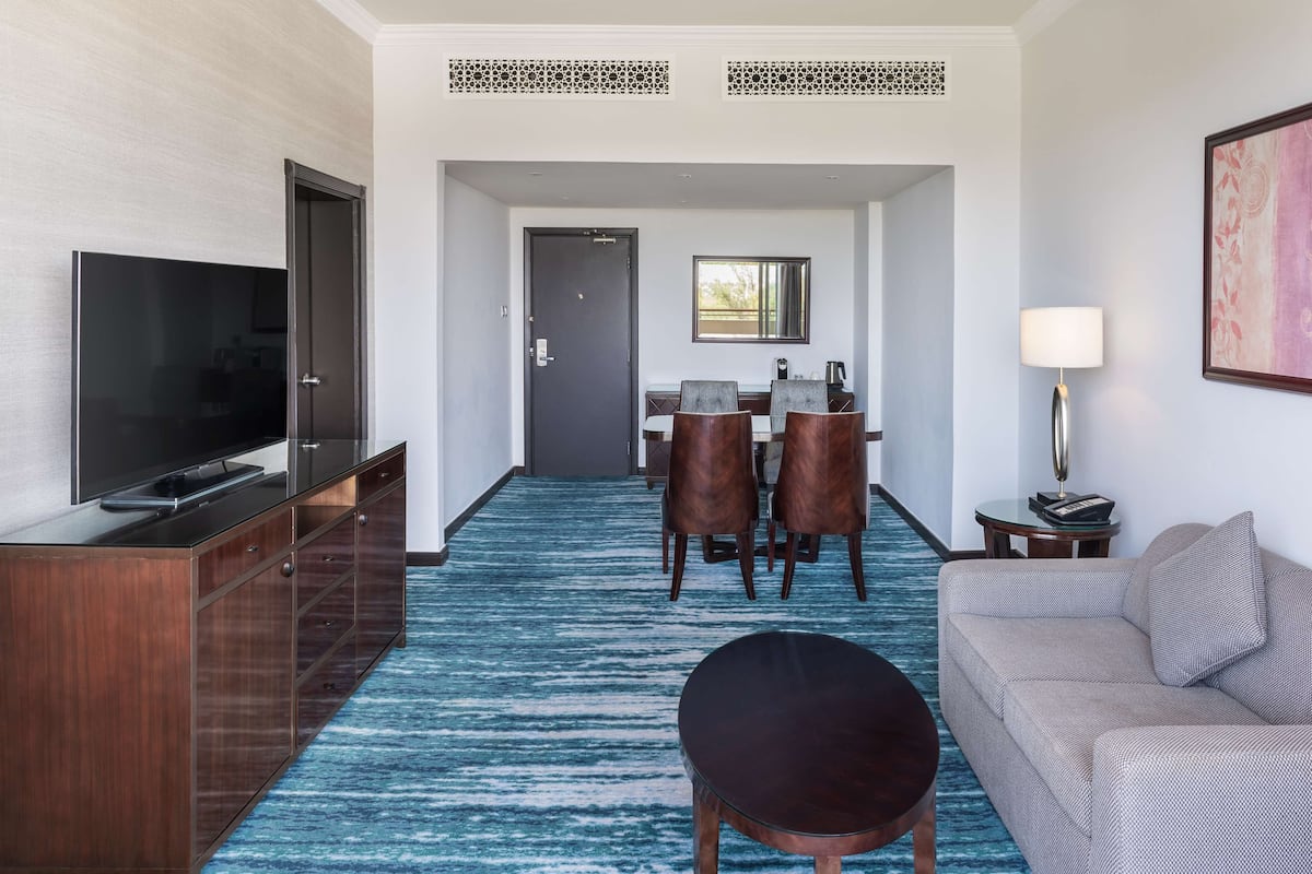 A hotel room with a TV, a dining area with chairs and a table, a sofa, and a lamp.