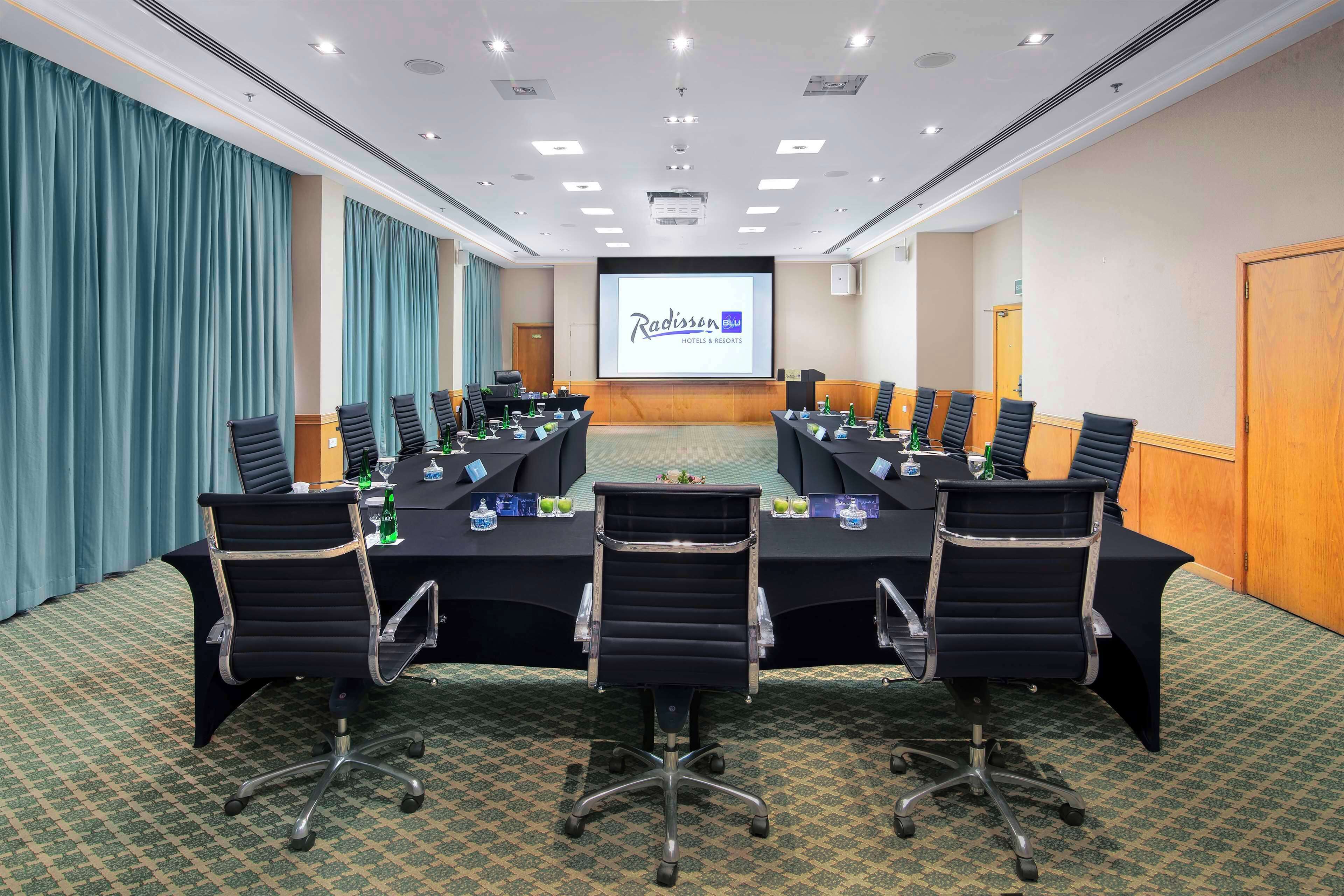 A conference room with a long table, black chairs, and a projector screen displaying "Radisson Hotels & Resorts".
