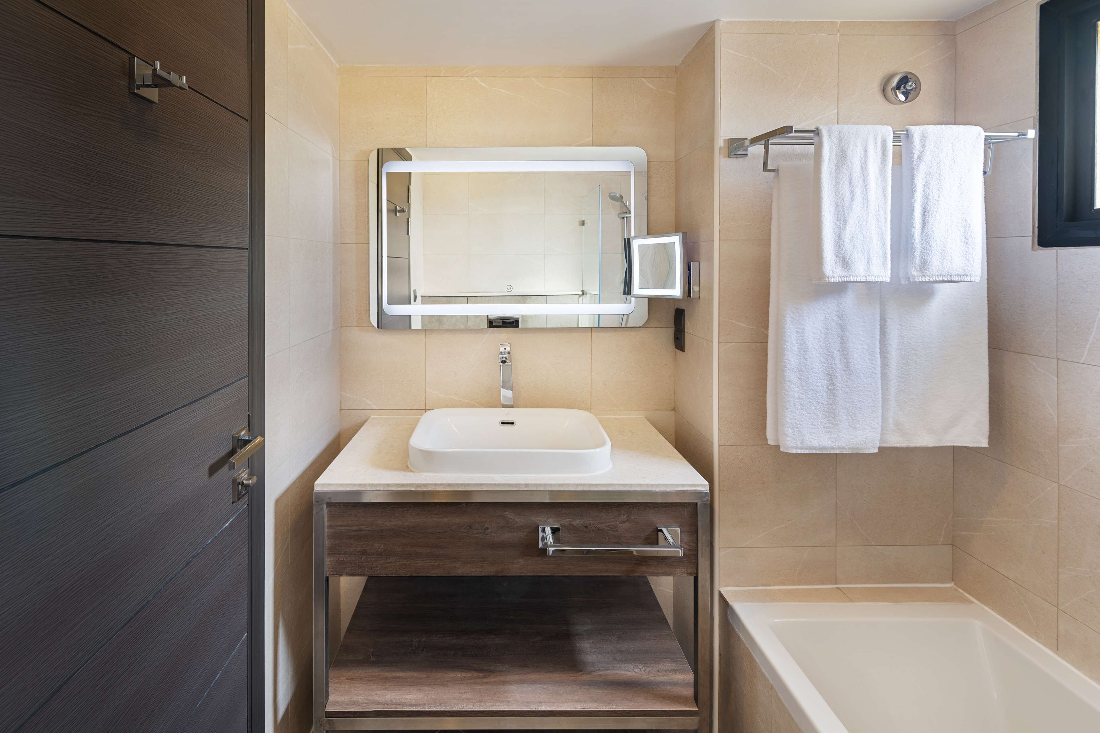 A modern bathroom with a large mirror, a sink, a vanity with a drawer, and a bathtub.