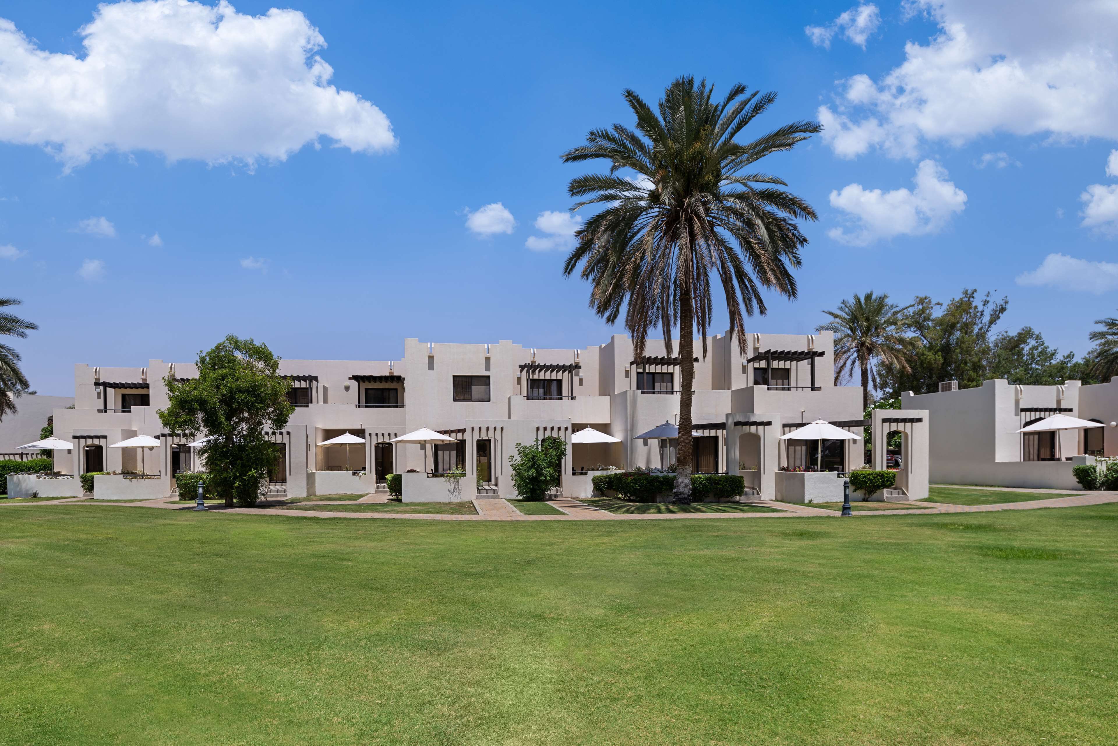 A modern hotel with a symmetrical facade, multiple balconies, and a well-maintained lawn.