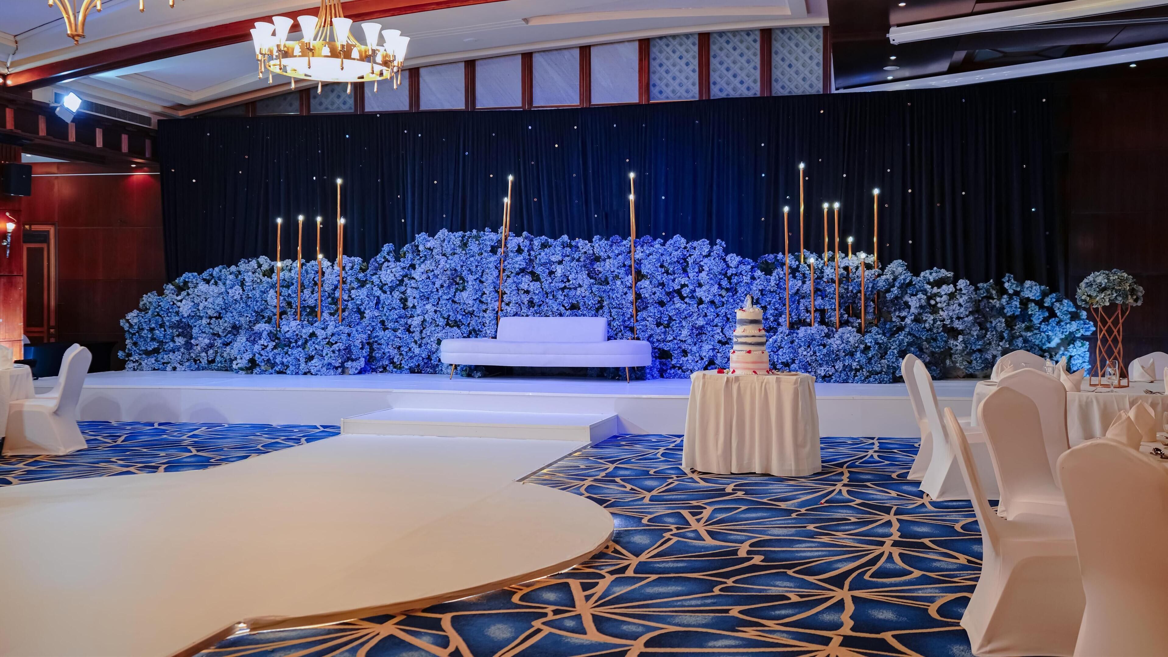 Un escenario con un sofá blanco, un pastel de varios niveles y un fondo floral.