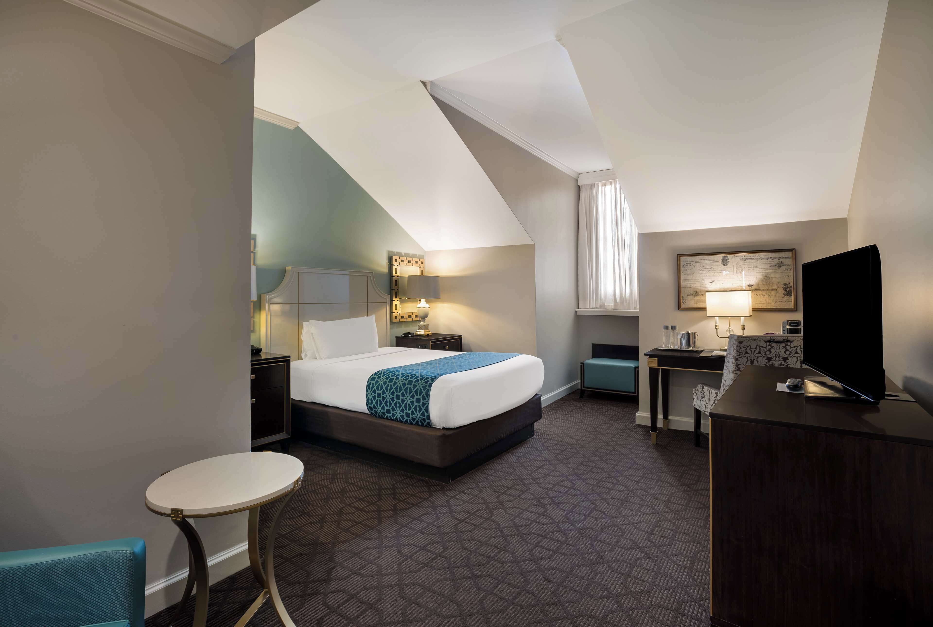 A hotel room with a bed, a desk, a chair, a television, and a small table.