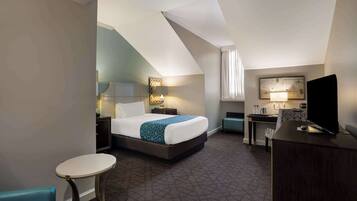 A hotel room with a bed, a desk, a chair, a television, and a small table.