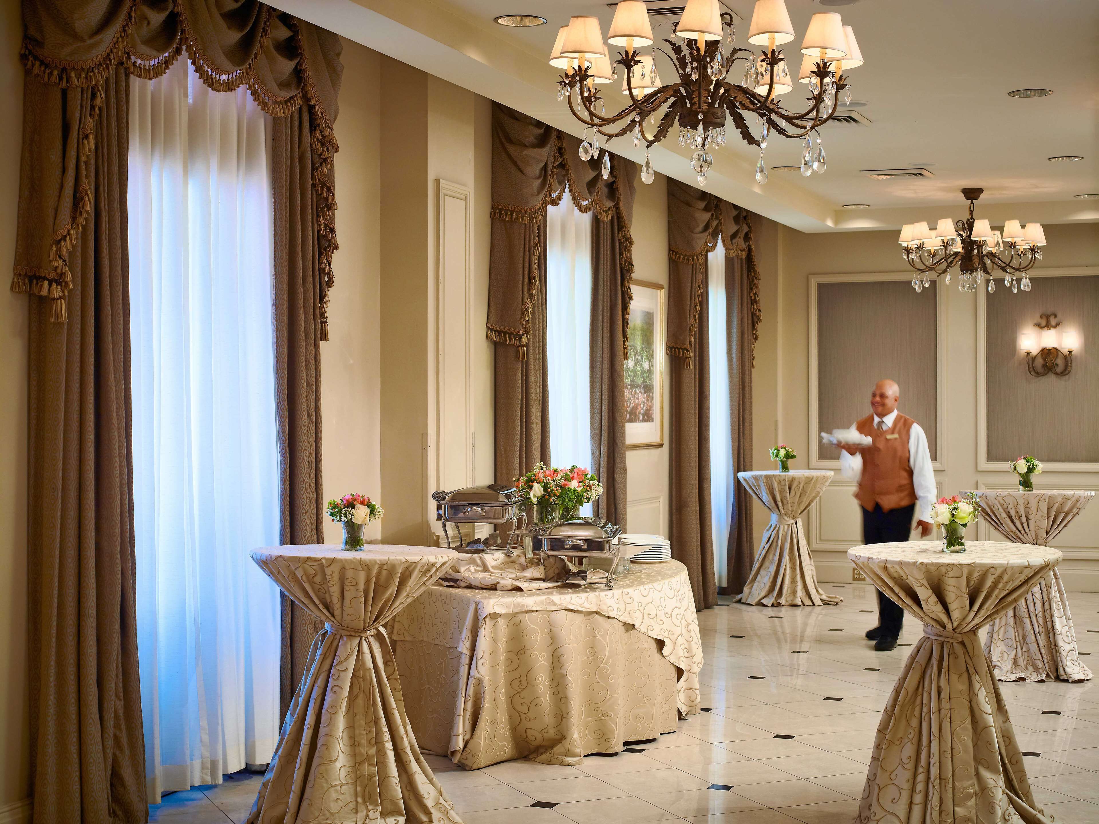 Espaço de refeições de hotel com mesas preparadas para o serviço, um candelabro e cortinas.