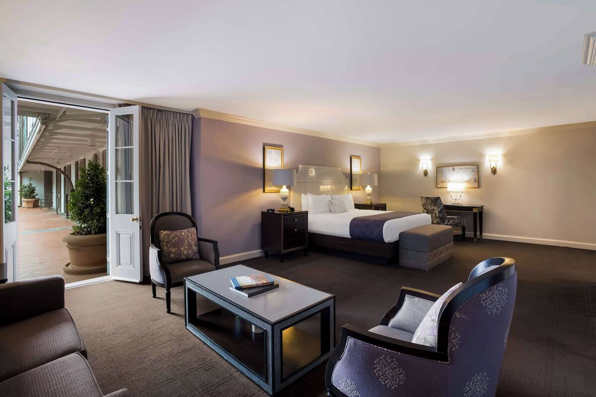 Ein Hotelzimmer mit einem Bett, einer Sitzecke mit Couchtisch, einem Sessel, einem Nachttisch und einer Lampe.