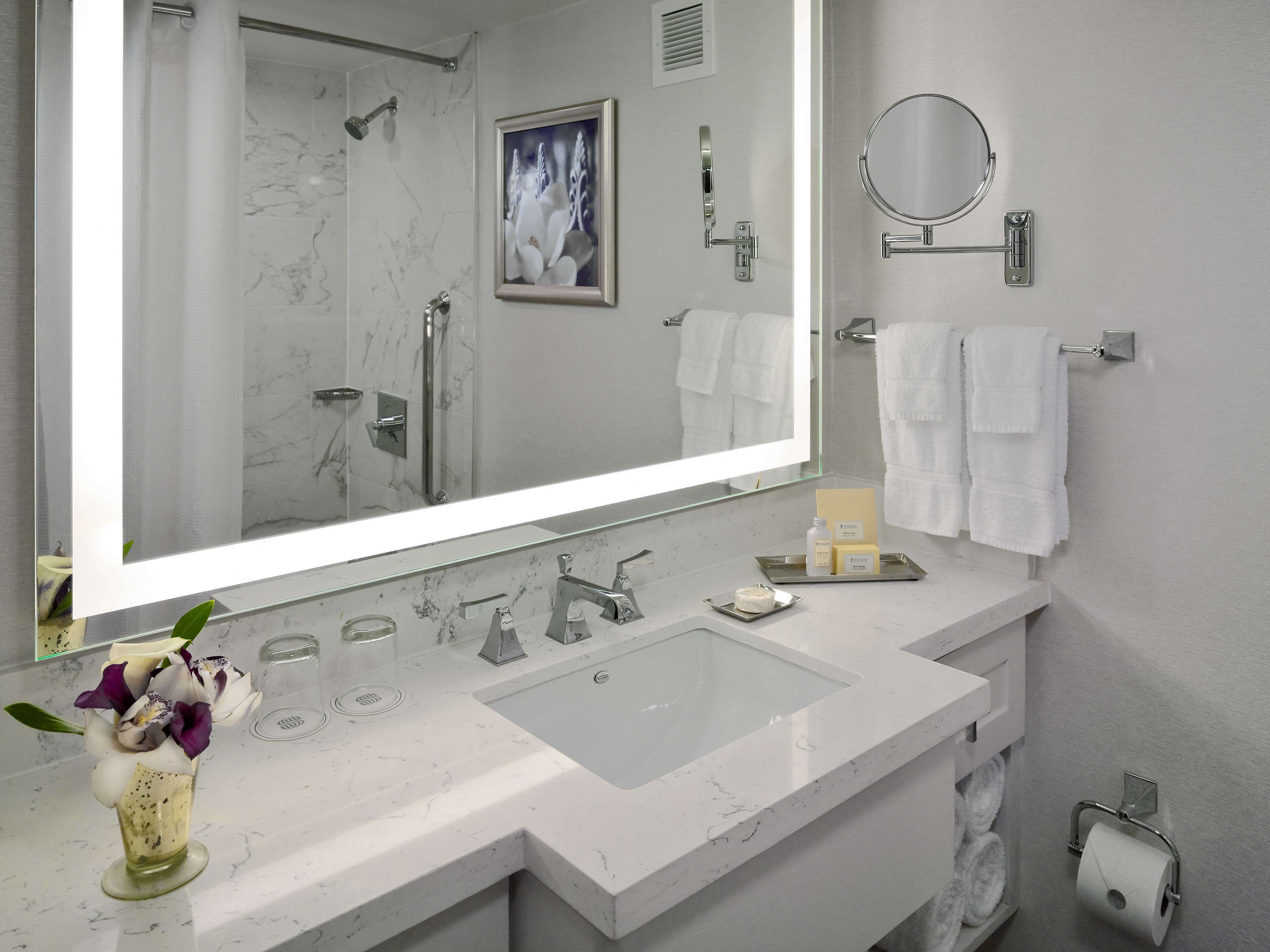 A modern bathroom with a large mirror, a shower, a sink with a vanity, and a towel rack.