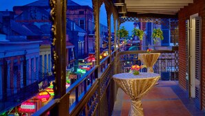 Ein Balkon mit Blick auf eine Stadtlandschaft im Abenddämmerung, mit Geländer, Tisch, einer Vase und Topfpflanzen.