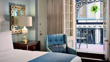 A hotel room with a bed, a chair, a nightstand, a lamp, a mirror, and a balcony with a view.