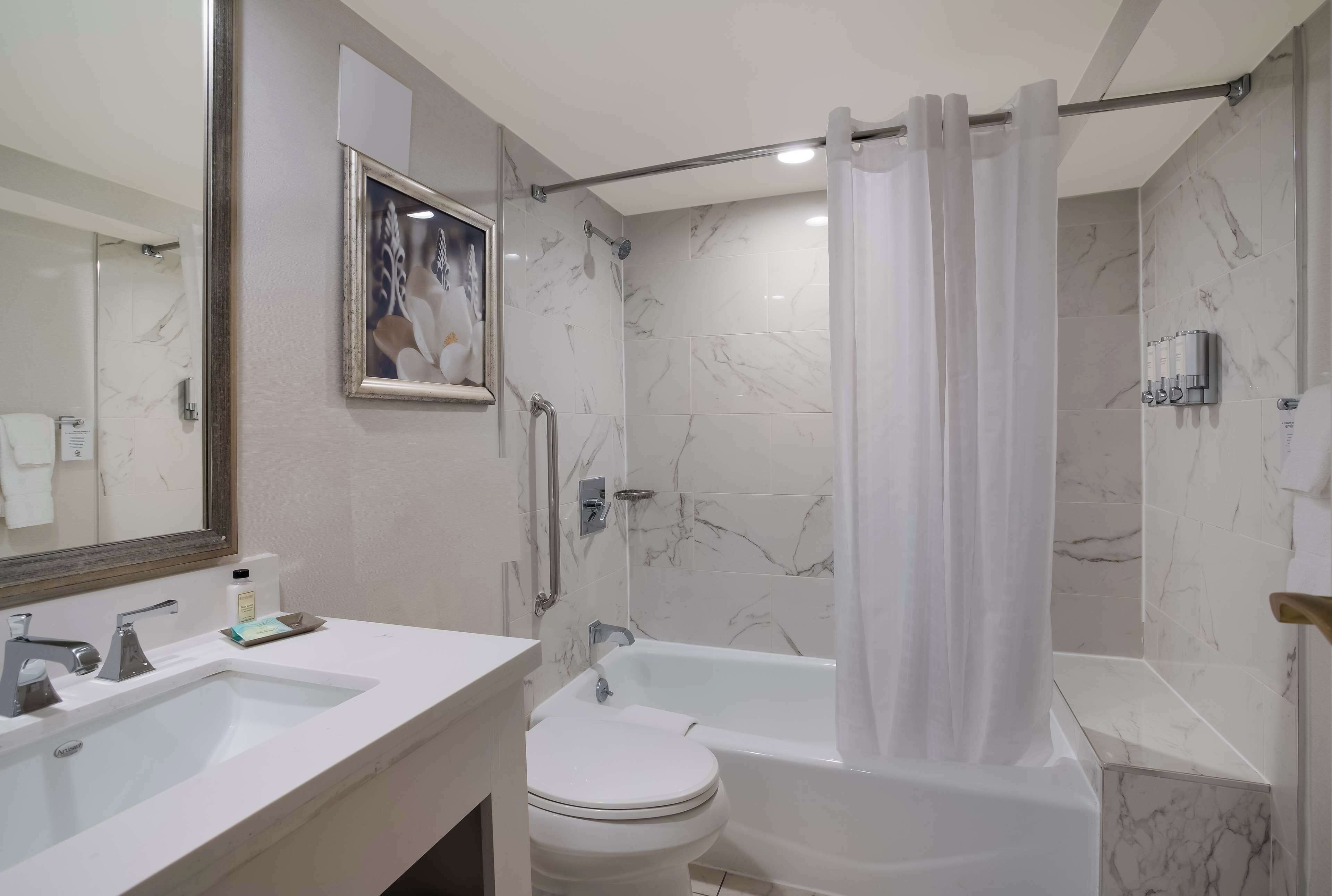 A bathroom with a bathtub, toilet, and sink, marble walls, and a shower curtain.