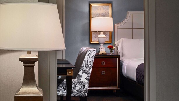 Ein Hotelzimmer mit einem Bett, einem Nachttisch mit Lampe, einem Sessel und einem Wandbild.