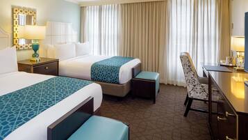 A hotel room with two beds, a desk, a chair, a lamp, and a mirror.