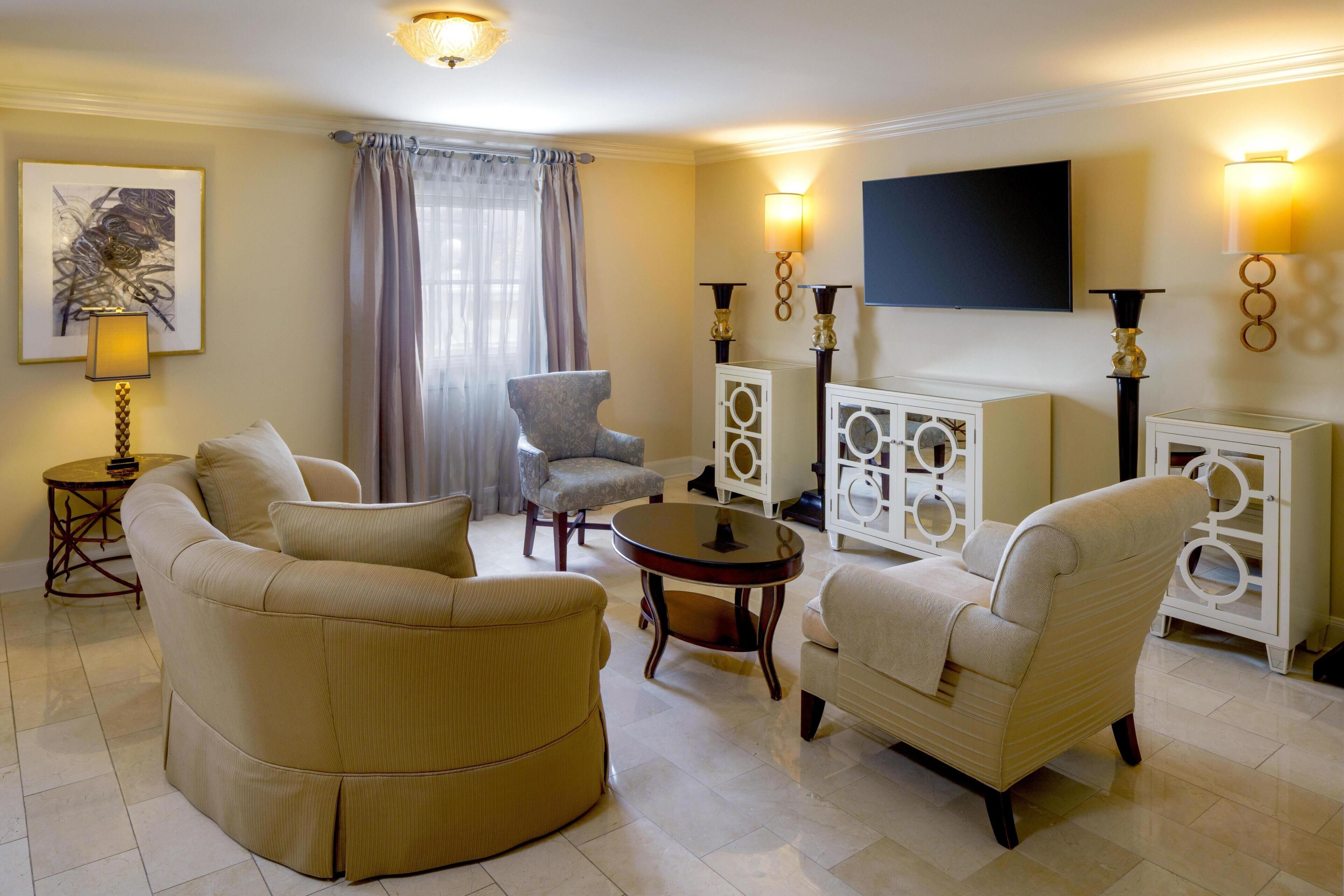 A living room with a sofa set, a round coffee table, a TV mounted on the wall, and decorative wall sconces.