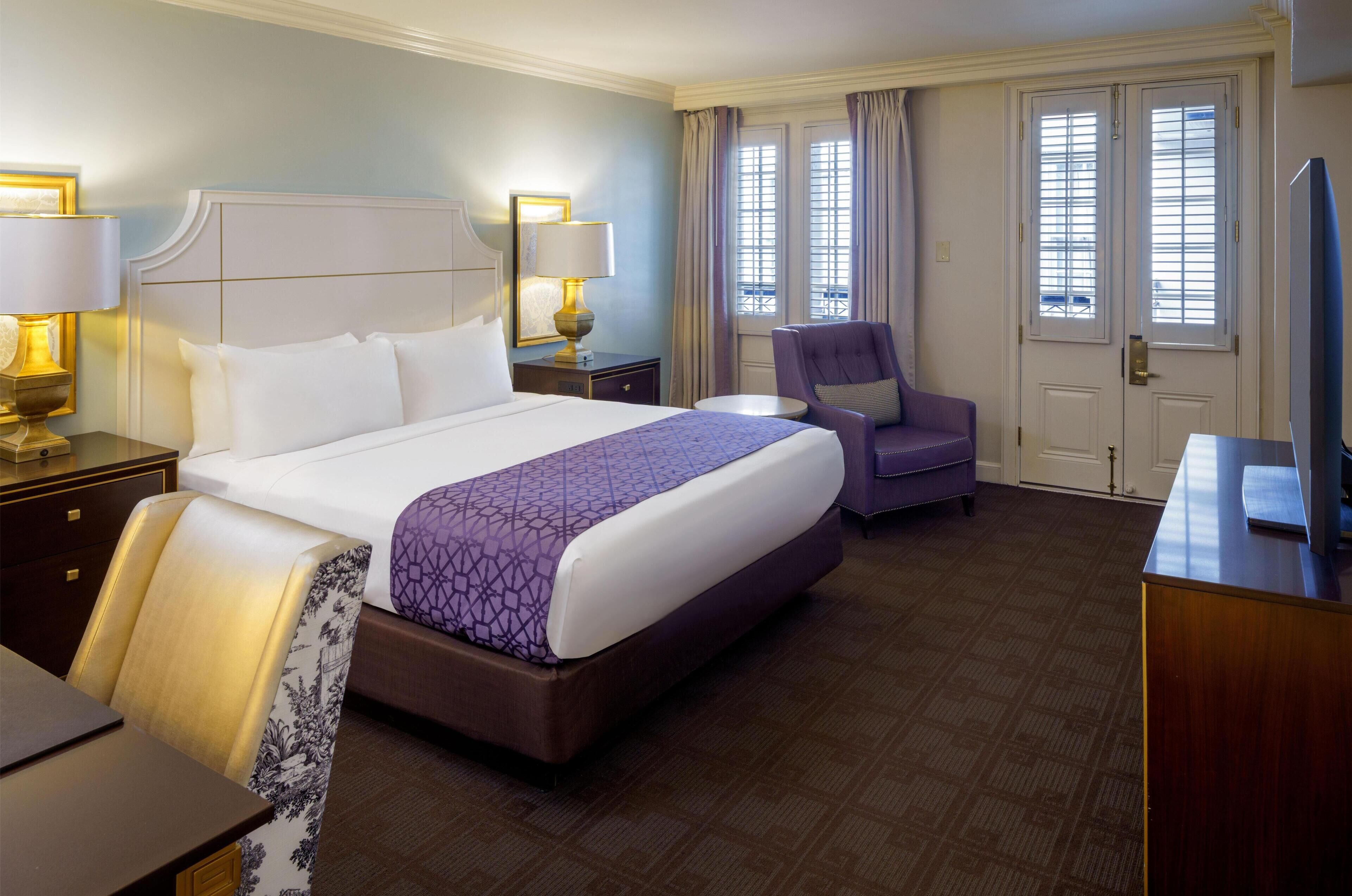 A hotel room with a large bed, a chair, a desk, and a television.
