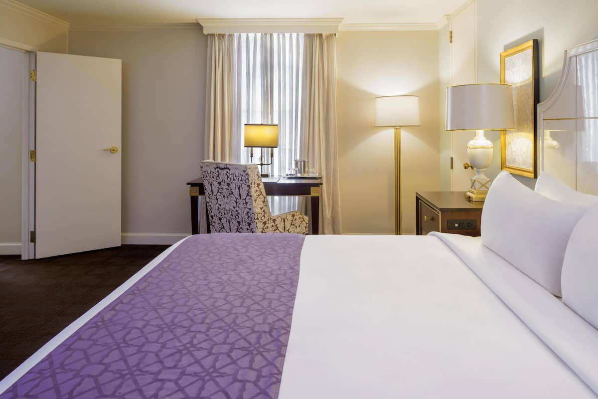 Ein Hotelzimmer mit einem großen Bett, einem Schreibtisch, einem Stuhl, einer Lampe und einer Tür.