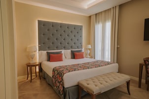 A hotel room with a large bed, two bedside tables with lamps, a bench, and a television on the wall.