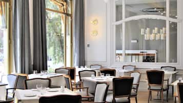 Comedor con mesas dispuestas para el servicio, ventanas amplias con cortinas y una lámpara moderna.