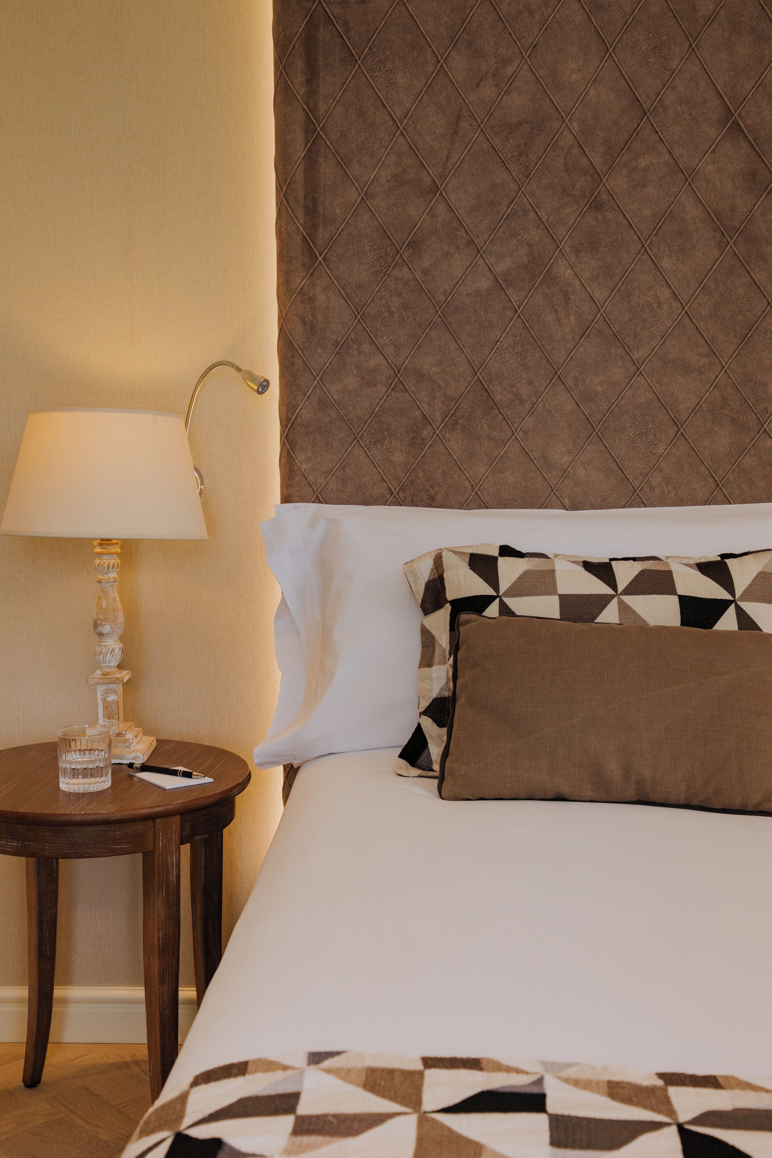 Una habitación de hotel con una cama, una mesita de noche con lámpara y un cojín decorativo.