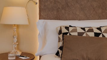 Una habitación de hotel con una cama, una mesita de noche con lámpara y un cojín decorativo.