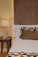 Una habitación de hotel con una cama, una mesita de noche con lámpara y un cojín decorativo.
