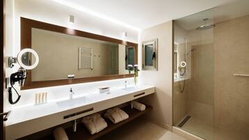 Un baño moderno con un espejo grande, lavamanos blanco y cabina de ducha de cristal.