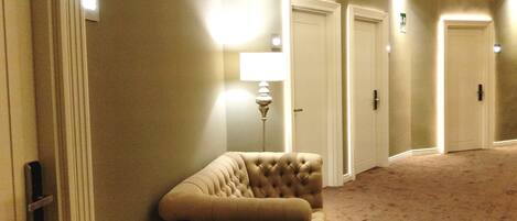 A hallway with a tufted armchair, a floor lamp, and three closed doors.