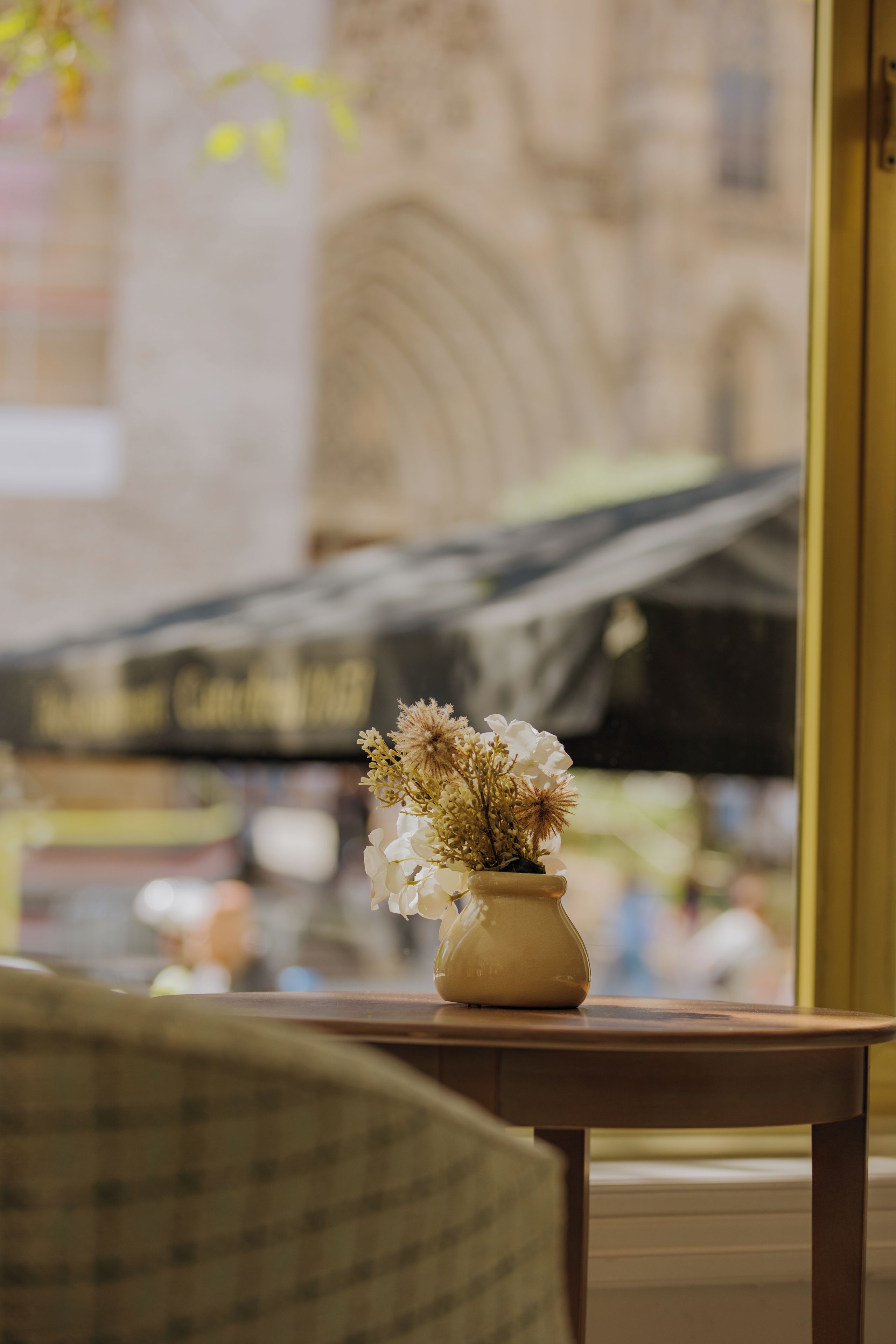 Un jarrón con flores sobre una mesa cerca de una ventana.