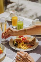 Aamiaispöytä, jolla on lautasellinen munia, paahtoleipää ja tomaatteja, lasi appelsiinimehua ja vihreää smoothiea.