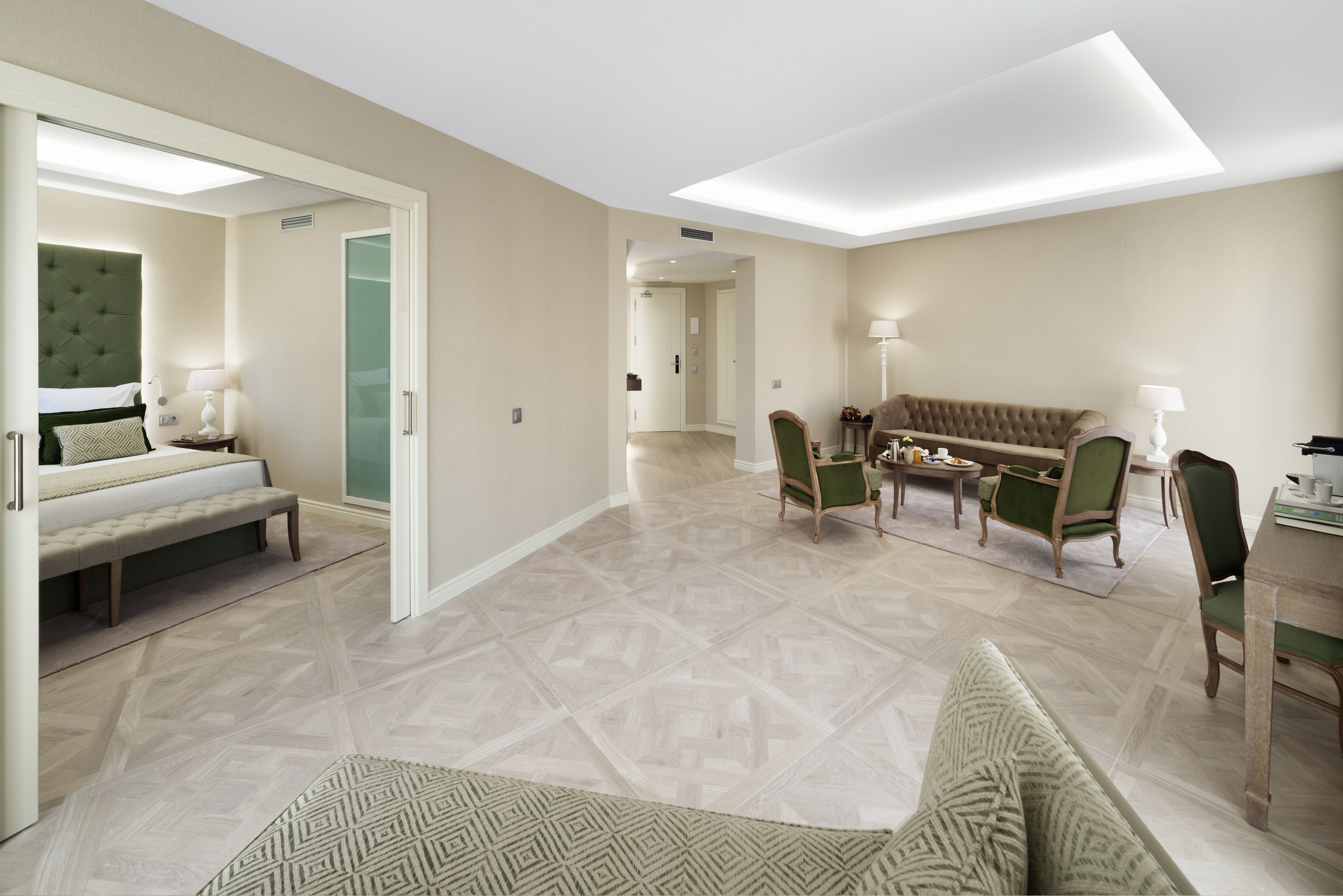 A hotel room with a bed, a sofa, a dining area, and a hallway.