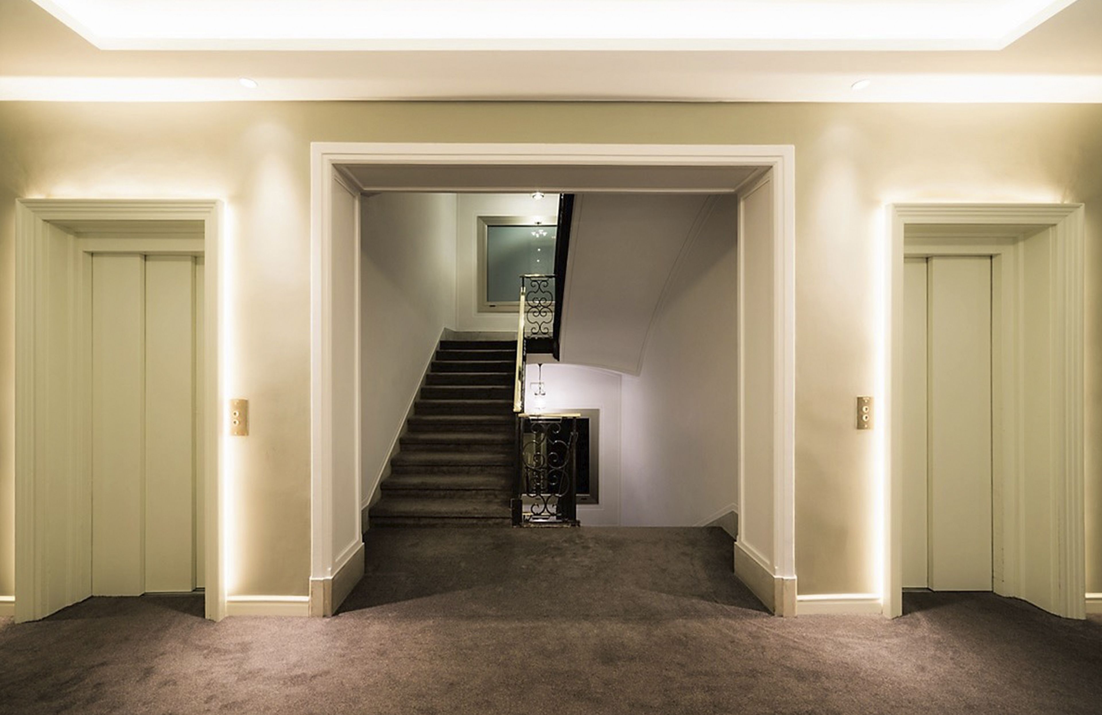 Un pasillo con pisos alfombrados, una escalera y una puerta con un panel decorativo.