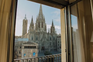 Vista de una catedral con múltiples agujas y un campanario a través de una ventana con barandilla de metal.