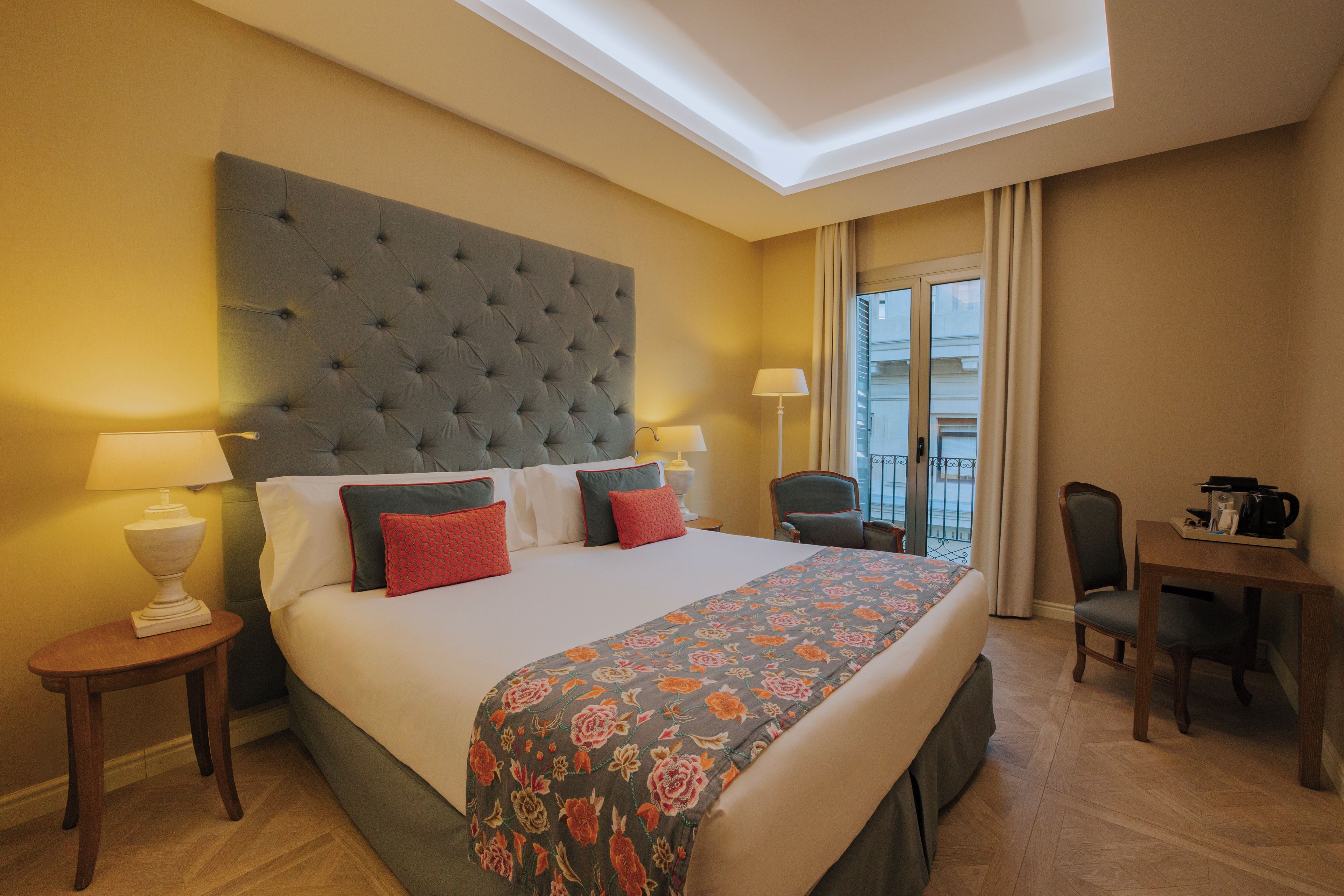 Quarto de hotel com uma cama grande, duas mesas de cabeceira, uma cadeira, uma escrivaninha e vista para o exterior.