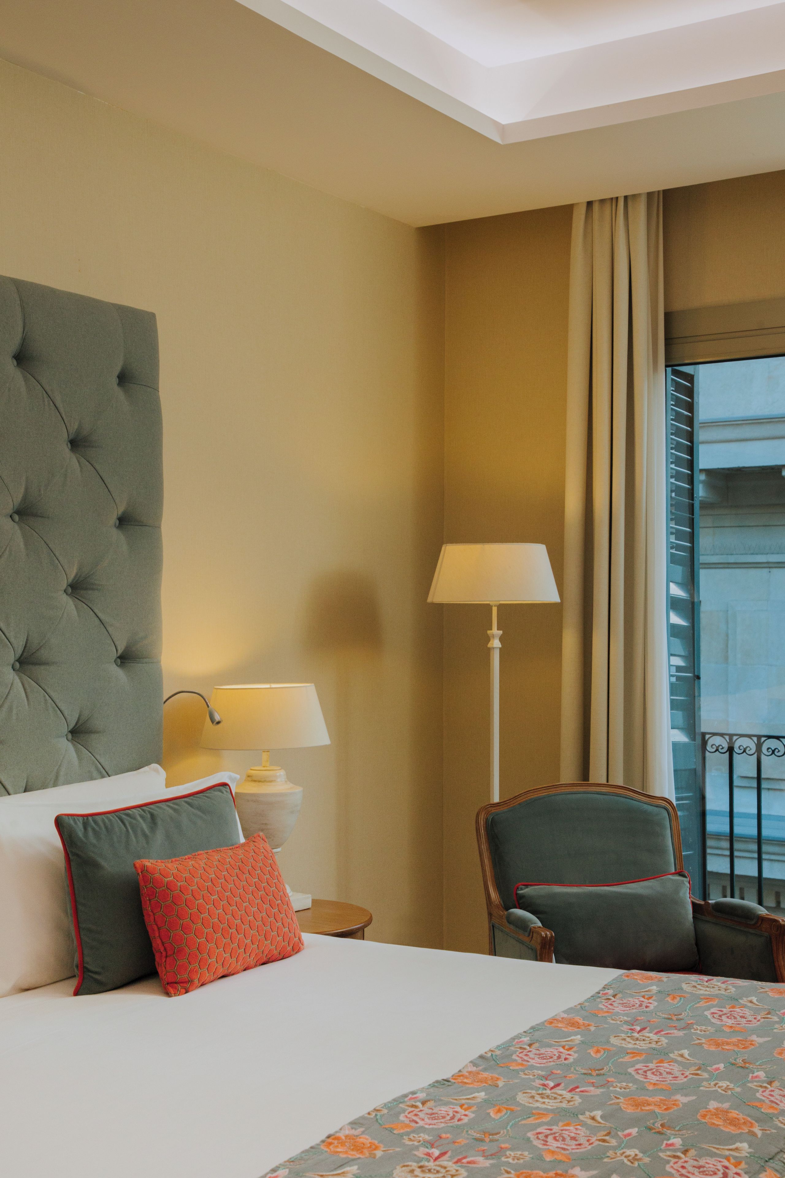 Habitación de hotel con una cama grande, una silla, una lámpara y vistas al exterior.