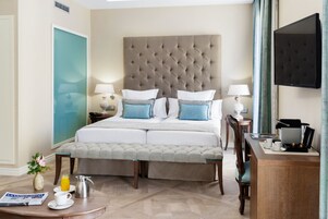 A hotel room with a large bed, bedside tables with lamps, a desk with a coffee maker, and a TV on the wall.