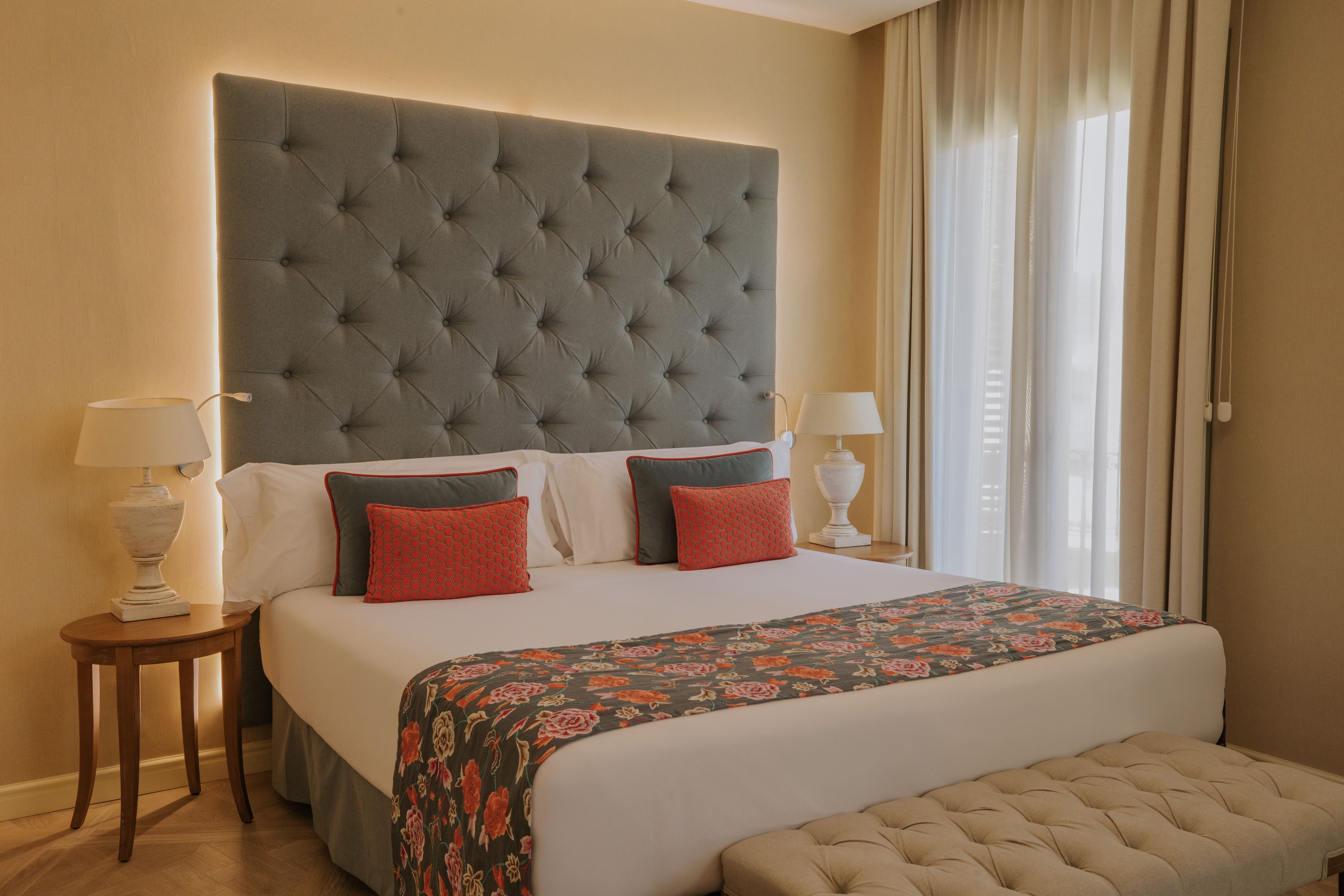 Una habitación de hotel con una cama grande, dos mesitas de noche y un banco.