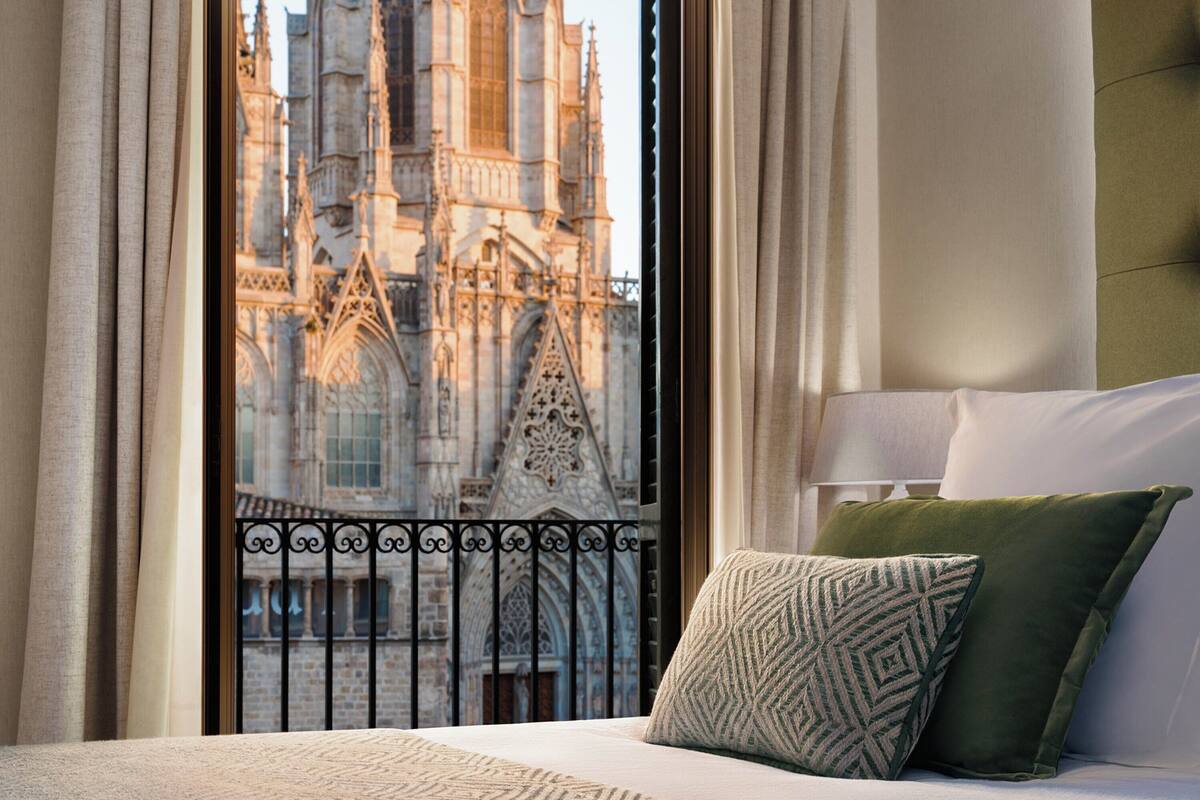 Quarto de hotel com vista para uma catedral gótica através de uma janela com cortinas.