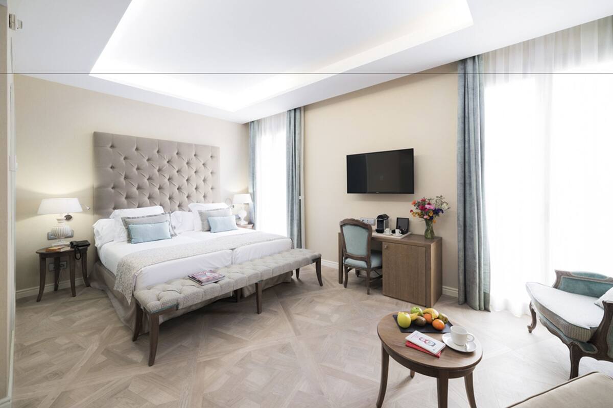 Quarto de hotel moderno com uma cama grande, uma escrivaninha, televisão de tela plana e um espaço de refeições com frutas.