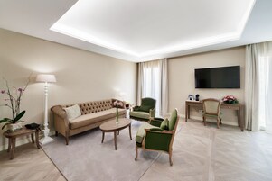 A modern living room with a sofa, armchairs, a coffee table, a TV, and a desk with a lamp and flowers.