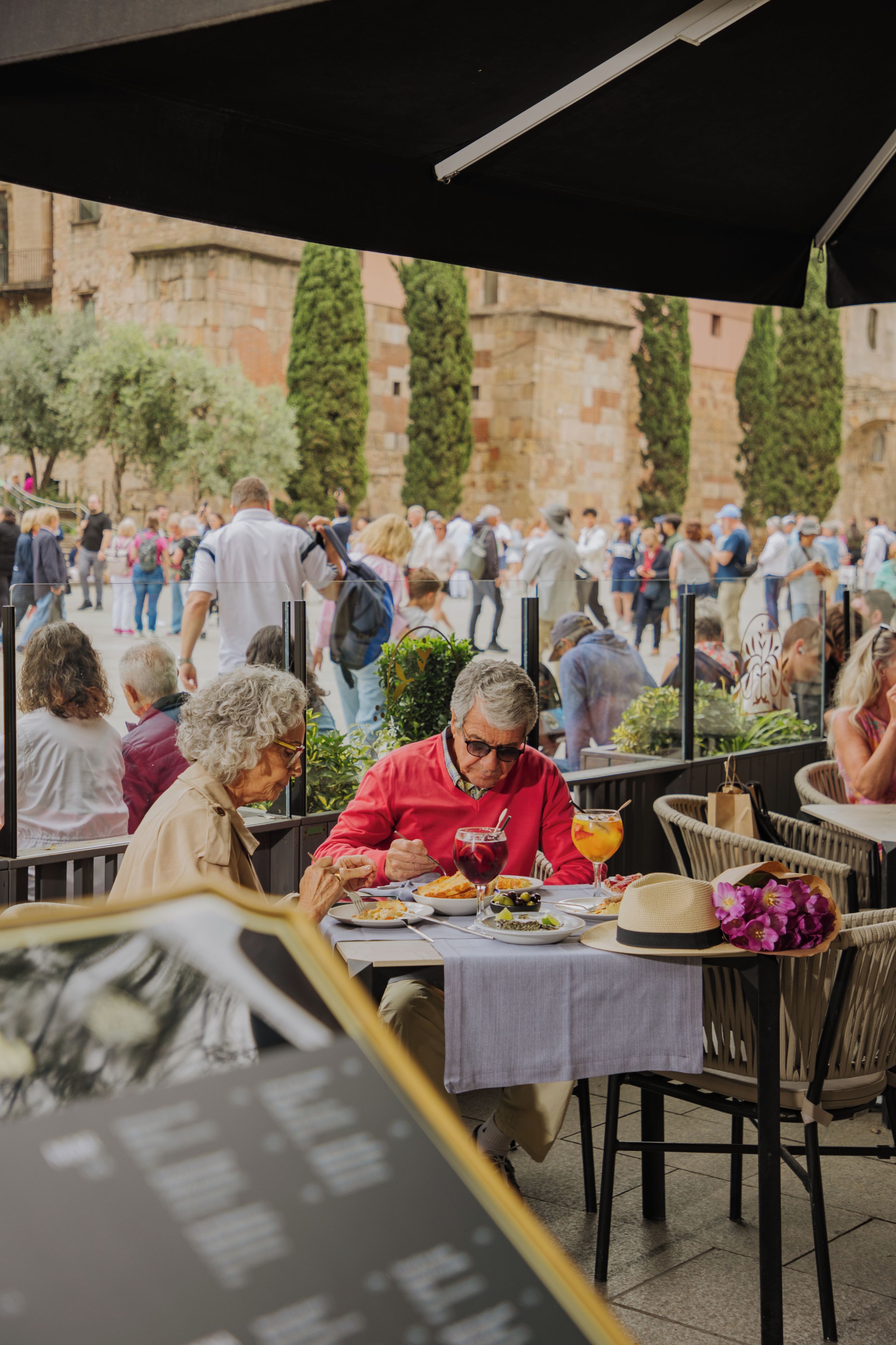 Un espace extérieur aménagé pour les repas, avec des tables et des chaises, entouré d’une foule de personnes.