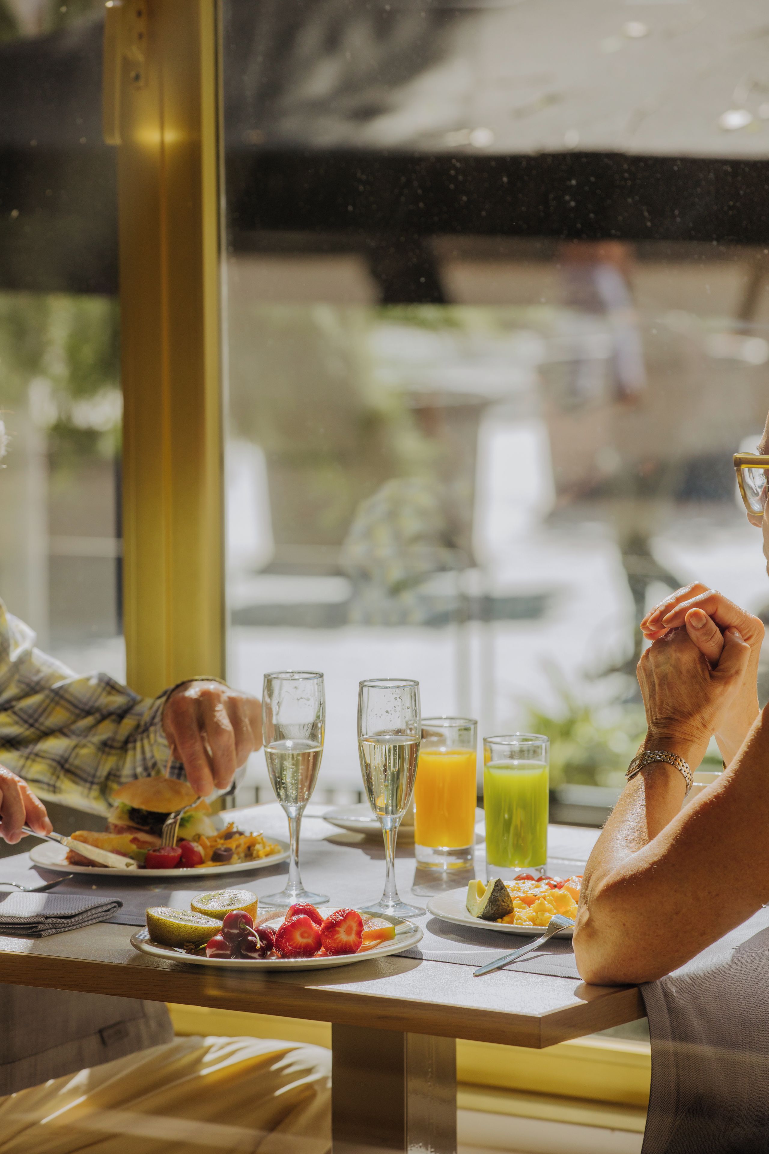 A dining table with plates of food, glasses of beverages, and a person holding hands.